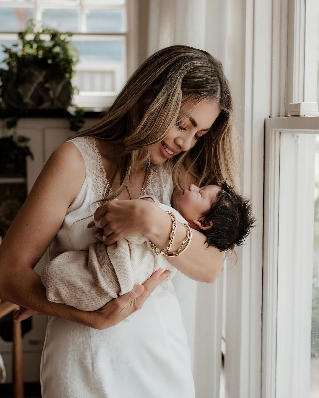 Mom lifting her newborn by a window
